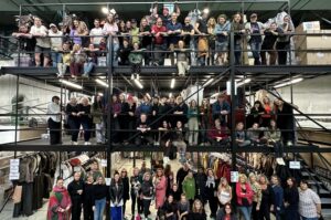 EXCLUSIVE: “The Wheel Of Time” Costume Designer Sharon Gilham Talks Season 3 1 A large group of people (The Wheel Of Time costume department) standing on three levels of a warehouse filled with costumes, all posing for a photo.